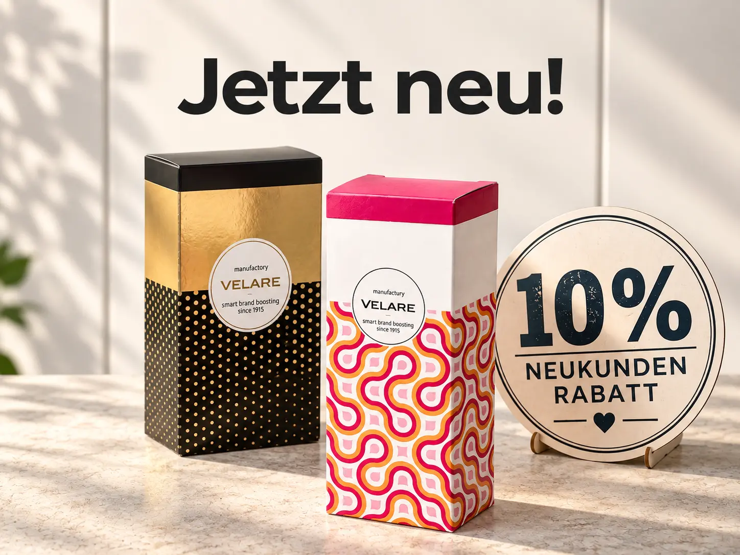 „Jetzt neu!“ – zwei individuell bedruckte Faltschachteln in Schwarz-Gold und Pink-Orange mit dem Hinweis „10 % Neukundenrabatt“. [KI-generiert]